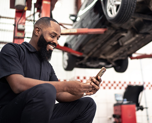 Auto mechanic business owner paying bills on his phone in the shop